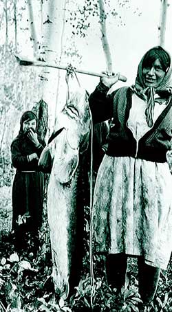 First Nations woman carrying a sturgeon on a stick